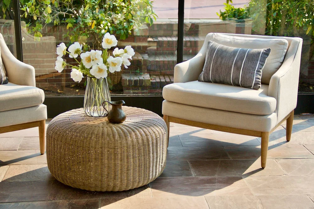 A cream lounge chair with a striped cushion beside a woven round table